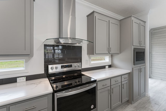 kitchen featuring wall chimney range hood, light stone counters, light hardwood / wood-style flooring, gray cabinets, and electric stove