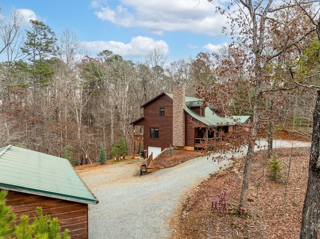 view of side of property with driveway, a chimney, and a forest view