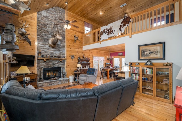 living room featuring a ceiling fan, wood ceiling, wood finished floors, a stone fireplace, and wood walls