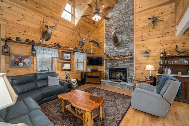 living area with ceiling fan, vaulted ceiling with skylight, wooden walls, a fireplace, and wood finished floors