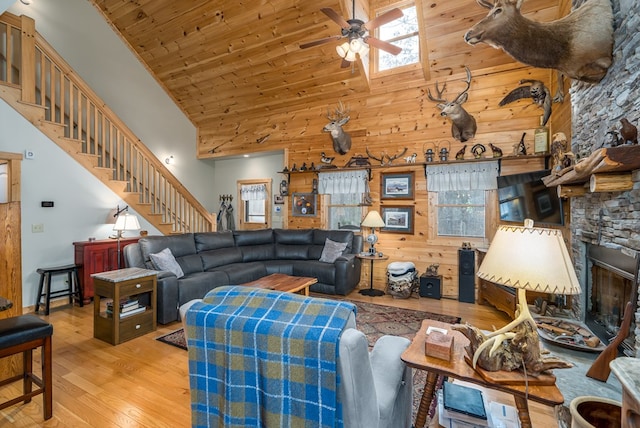 living area with a towering ceiling, a ceiling fan, wood finished floors, wooden ceiling, and stairs