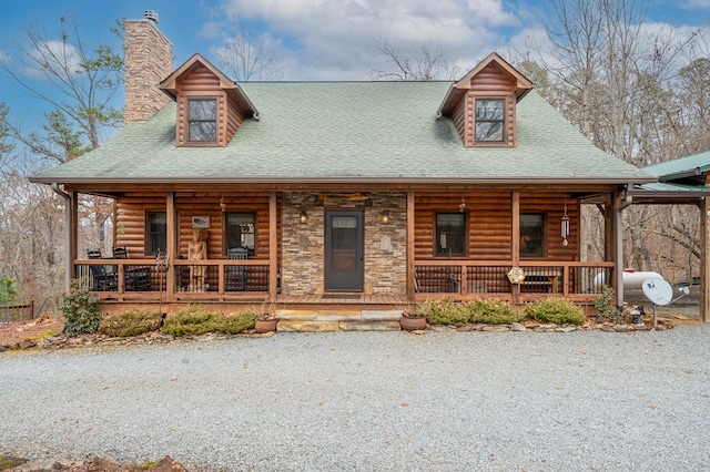 log home with stone siding, a chimney, a porch, and roof with shingles