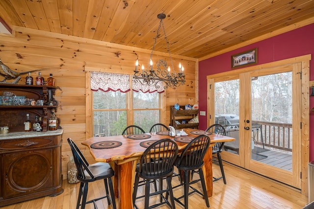 dining space featuring french doors, wooden walls, a chandelier, light wood-type flooring, and wooden ceiling