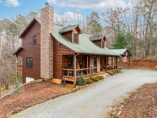 view of front of home with covered porch, driveway, roof with shingles, a chimney, and log veneer siding