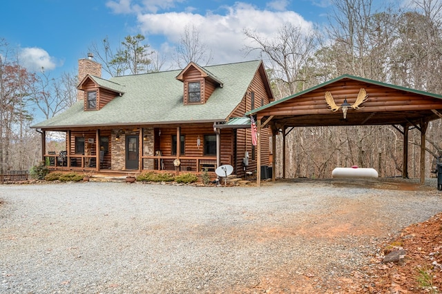 cabin featuring covered porch, driveway, a chimney, and a detached carport