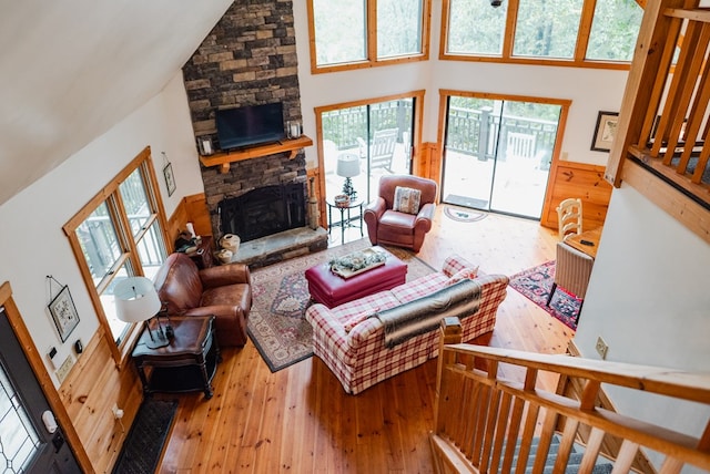 living room with wood-type flooring, high vaulted ceiling, and a stone fireplace