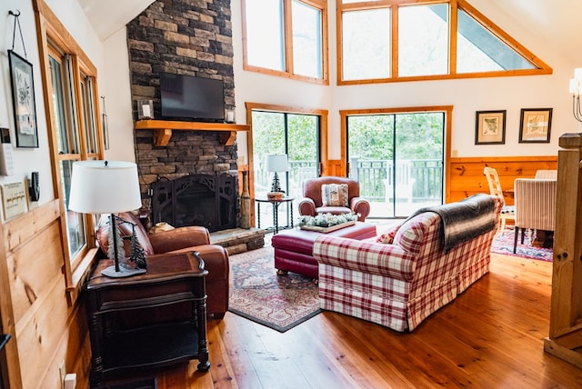 living room with a stone fireplace, high vaulted ceiling, and hardwood / wood-style flooring