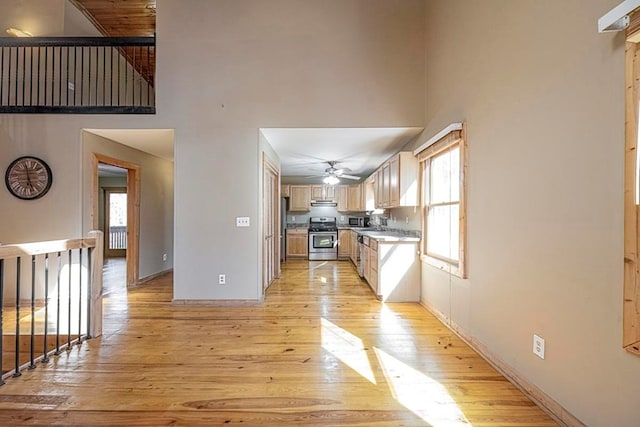 kitchen with appliances with stainless steel finishes, a towering ceiling, light brown cabinetry, ceiling fan, and light hardwood / wood-style flooring