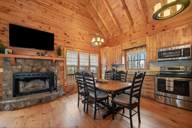 dining room with a fireplace, wood ceiling, light wood-style floors, wood walls, and beamed ceiling