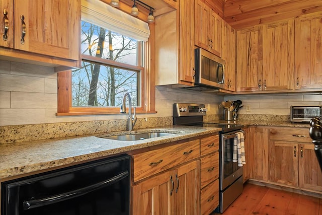 kitchen featuring light stone counters, light wood finished floors, a sink, appliances with stainless steel finishes, and tasteful backsplash