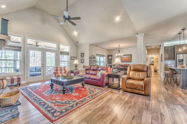 living room with ornate columns, french doors, light wood-style floors, high vaulted ceiling, and ceiling fan with notable chandelier