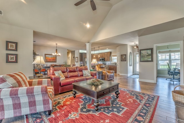 living room with high vaulted ceiling, ceiling fan with notable chandelier, wood finished floors, visible vents, and baseboards