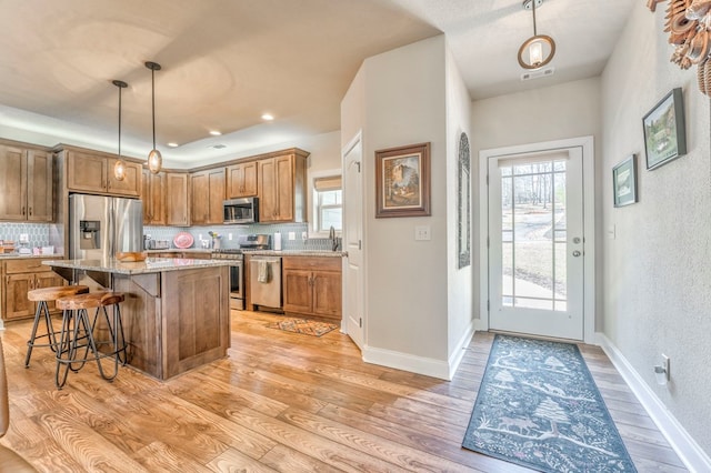 kitchen featuring stainless steel appliances, hanging light fixtures, brown cabinetry, and a kitchen island