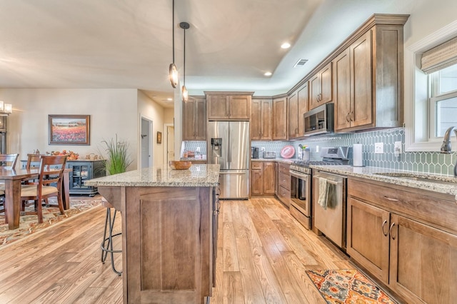 kitchen with brown cabinetry, light stone countertops, stainless steel appliances, pendant lighting, and a sink