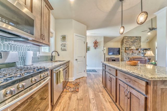 kitchen featuring brown cabinetry, light stone counters, stainless steel appliances, pendant lighting, and a sink