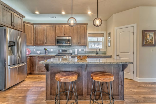 kitchen with visible vents, stainless steel appliances, light stone countertops, and a center island