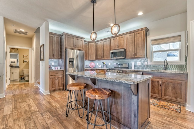 kitchen featuring stainless steel appliances, a kitchen island, light stone countertops, a kitchen bar, and pendant lighting