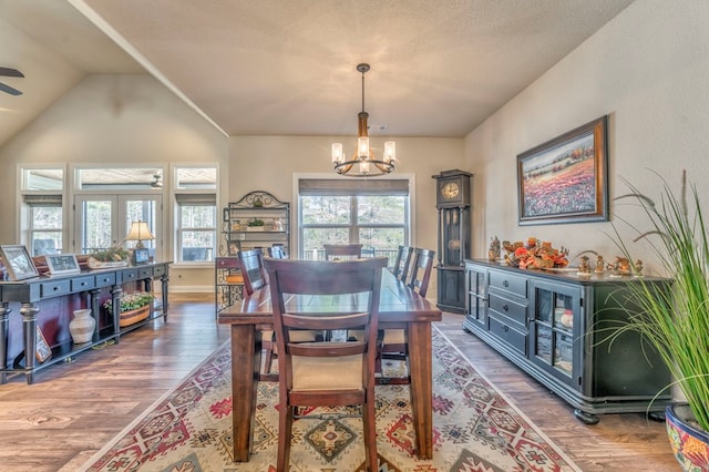 dining area featuring lofted ceiling, ceiling fan with notable chandelier, dark wood-style flooring, baseboards, and french doors