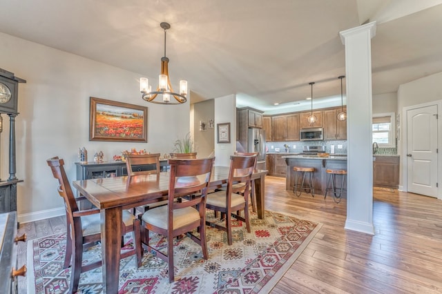 dining area featuring a chandelier, light wood finished floors, baseboards, and ornate columns