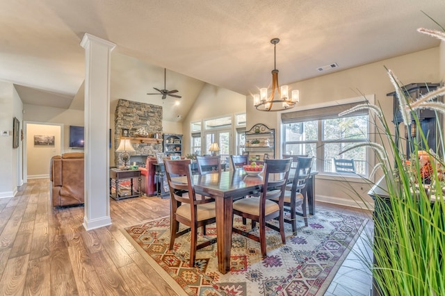 dining room featuring visible vents, wood finished floors, vaulted ceiling, ornate columns, and a fireplace