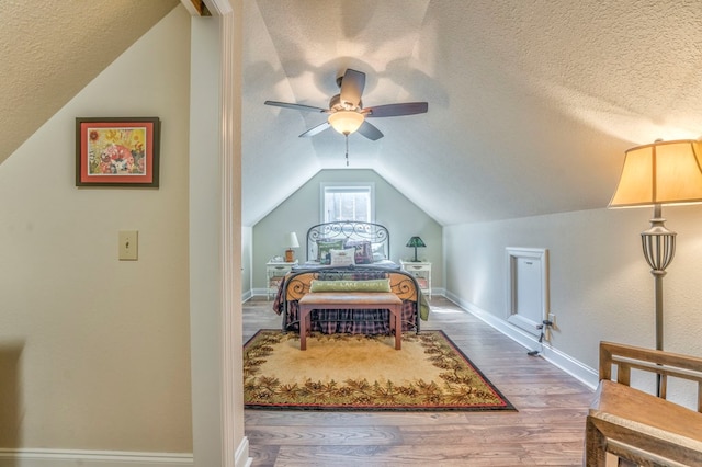 bedroom with a textured ceiling, ceiling fan, wood finished floors, baseboards, and vaulted ceiling