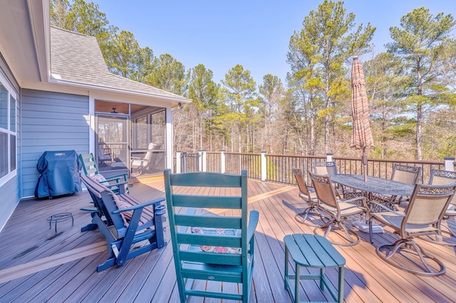 wooden terrace with outdoor dining space, a grill, and a sunroom