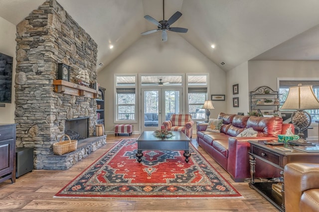 living room featuring high vaulted ceiling, a stone fireplace, a ceiling fan, and light wood-style floors