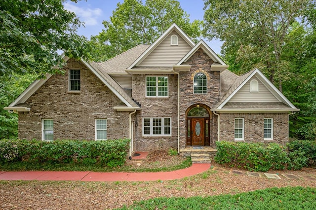 view of front facade featuring brick siding, stone siding, and roof with shingles