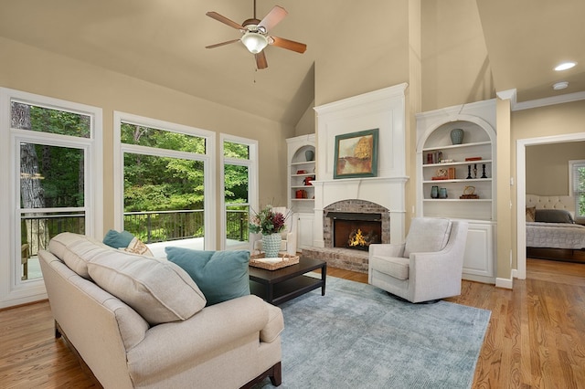 living room featuring built in features, a ceiling fan, high vaulted ceiling, light wood-style flooring, and a brick fireplace