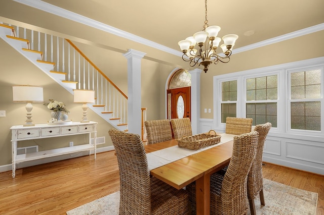 dining space featuring crown molding, wood finished floors, stairs, and ornate columns