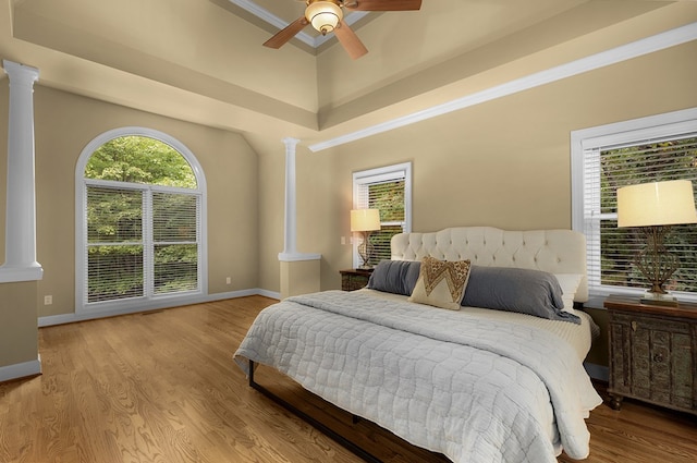 bedroom with ceiling fan, wood finished floors, baseboards, and decorative columns