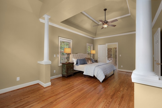 bedroom featuring light wood finished floors, crown molding, baseboards, a tray ceiling, and ornate columns