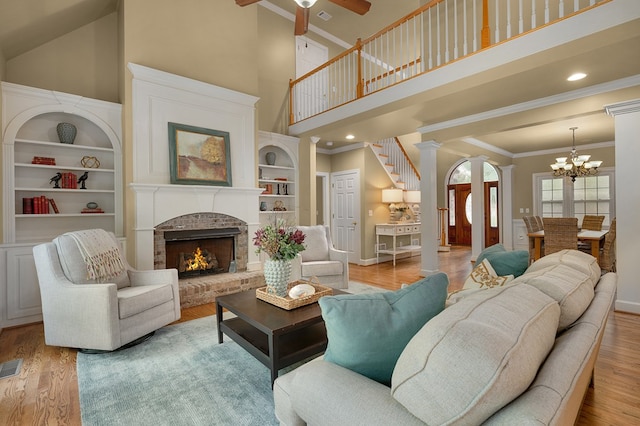 living room with ornamental molding, wood finished floors, decorative columns, a brick fireplace, and a towering ceiling