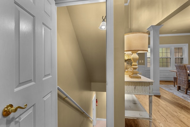 staircase featuring wood finished floors, crown molding, and decorative columns