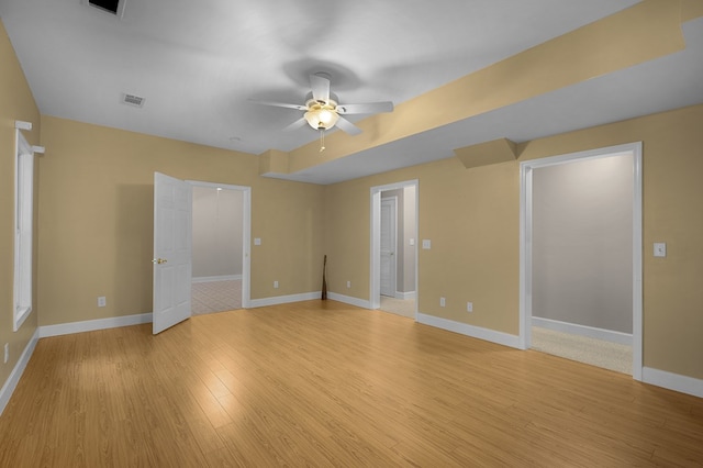 spare room featuring light wood finished floors, visible vents, a ceiling fan, and baseboards