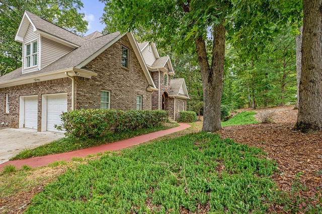 view of side of property featuring an attached garage, brick siding, roof with shingles, and driveway