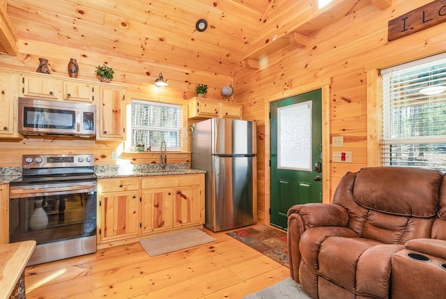 kitchen featuring light stone counters, appliances with stainless steel finishes, light wood-style floors, a sink, and wooden walls