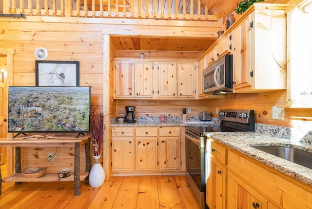 kitchen with light stone countertops, light wood-style flooring, stainless steel appliances, and wood walls