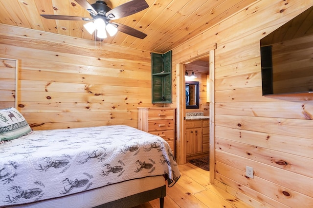 bedroom featuring a ceiling fan, connected bathroom, wood ceiling, light wood-style flooring, and wood walls
