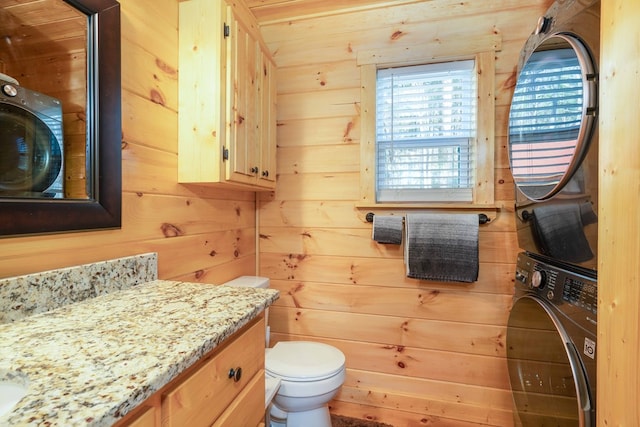 half bathroom featuring toilet, stacked washer and dryer, vanity, and wood walls