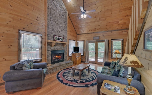 living room with a fireplace, high vaulted ceiling, wood walls, ceiling fan, and french doors