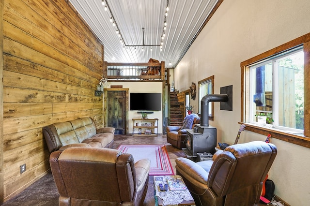 living room with wood walls, a towering ceiling, rail lighting, and a wood stove