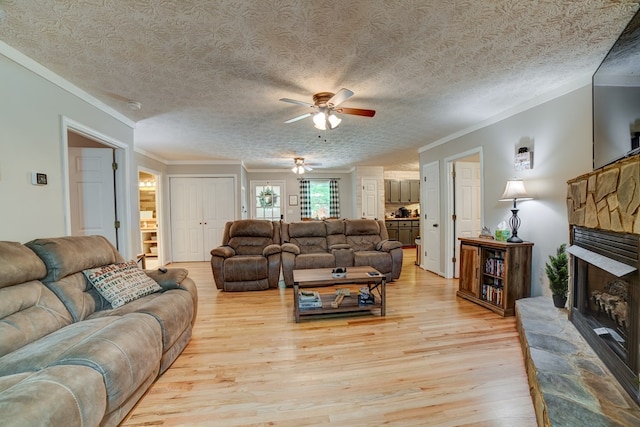 living room featuring a textured ceiling, ceiling fan, crown molding, light hardwood / wood-style flooring, and a fireplace