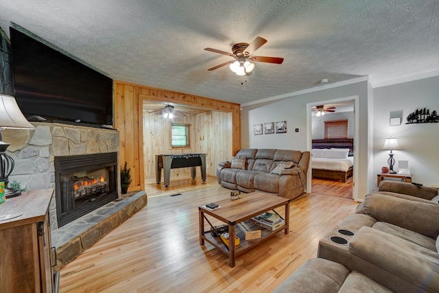 living room featuring ceiling fan, light hardwood / wood-style flooring, crown molding, wooden walls, and a fireplace