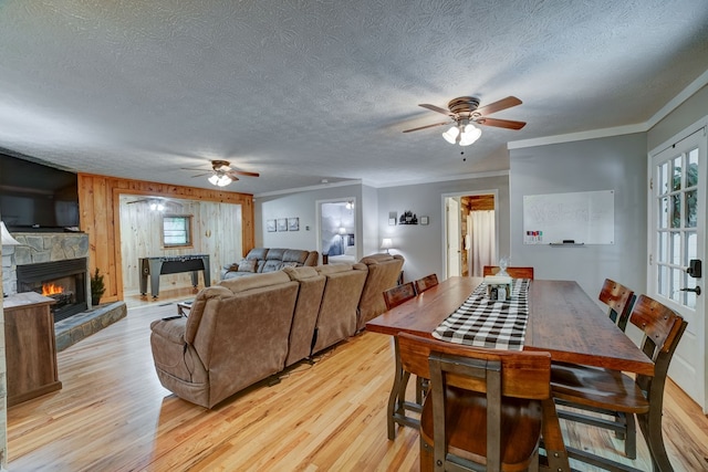 dining area featuring light wood-type flooring, a stone fireplace, ceiling fan, and crown molding