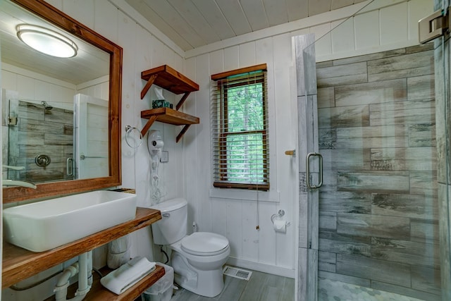 bathroom featuring wood walls, toilet, a shower with door, and sink