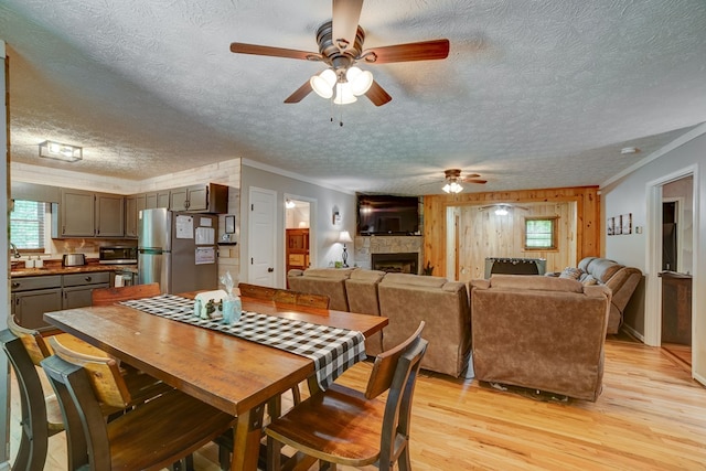 dining room with a fireplace, light wood-type flooring, ceiling fan, and ornamental molding