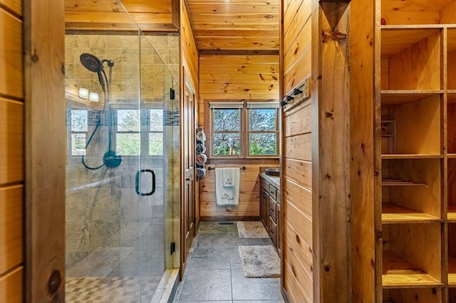 full bathroom featuring a shower stall, stone tile floors, wooden walls, and vanity