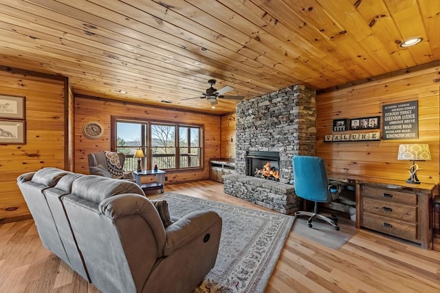 living room with wood walls, a stone fireplace, wood ceiling, and a ceiling fan