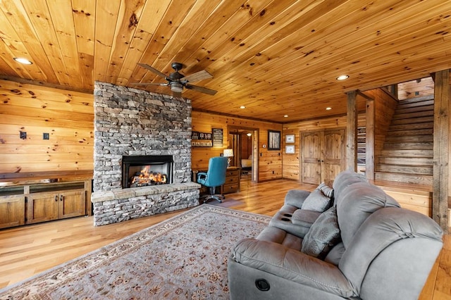 living room with a stone fireplace, recessed lighting, wood walls, ceiling fan, and wood finished floors